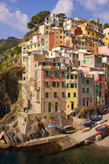 Fototapeta na wymiar Italy, Liguria region, Cinque Terre, Riomaggiore. Late afternoon sun on stacked buildings and harbor. 