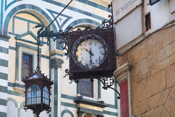 Fototapeta na wymiar Italy, Florence. Wrought-iron clock and hanging lantern.