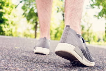Athlete walking on the road in the Park in the summer, the man's feet in sneakers, closeup, cropped image, toned. The concept of Hiking