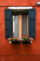 Fototapeta na wymiar Venice, Veneto, Italy - Black wooden shutters and flowers in a planter frame a window.