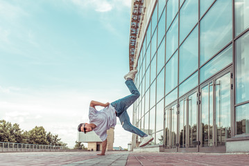 athlete man dancer white T-shirt jeans, jump on his arm, summer city, with glasses, background glass windows, active hip hop, youth lifestyle, acrobatic stunt break dance, street fashionable artist,