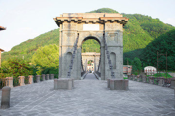Fototapeta premium Bagni di Lucca, Tuscany, Italy - An arch acting as an entrance to an old bridge. A hillside is viewable in the background.
