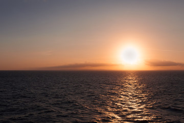 Sun about to set behind the horizon on the sea with italian coastline background