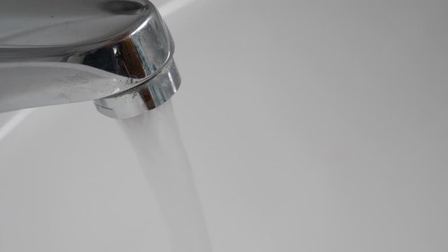 Tramsparent water running from chromium plated or metal tap into white sink in bathroom. Slow motion close-up shot. No people. Continious off on.