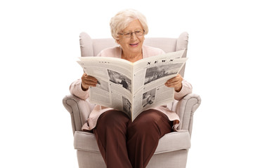 Senior lady sitting in an armchair and reading a newspaper