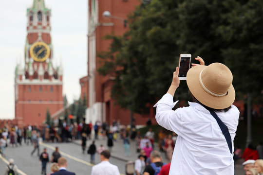 Woman tourist taking pictures of Moscow Kremlin on smartphone in summer. Crowd of tourists on the Red square, travel in Russia