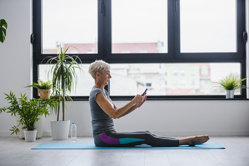 Senior woman using smartphone at home after exercise. The use of technology by the elderly.