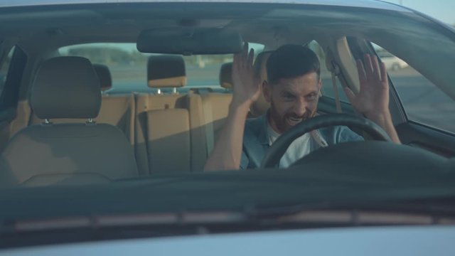 Young man driver beginner confused of failure first time driving in the car. Exhausted guy hitting steering wheel getting angry having problem.