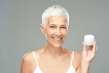 Gorgeous smiling Caucasian senior woman trying out new anti age cream and looking at camera. Beauty photography.