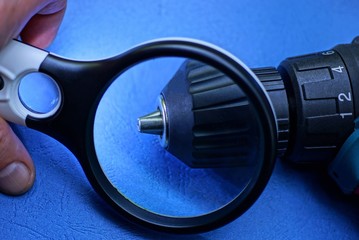 black magnifier in hand enlarges part of a screwdriver on a blue table