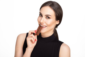 portrait of beautiful young lady with a charming smile eating chocolate in black dress on white background