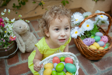 Fototapeta na wymiar Little girl in yellow Easter dress holding Easter basket full of colorful speckled Easter eggs. Blurred background.