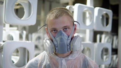 Portrait of a man in a mask in the paint shop. He is wearing a protective mask and a protective robe, he looks at the camera