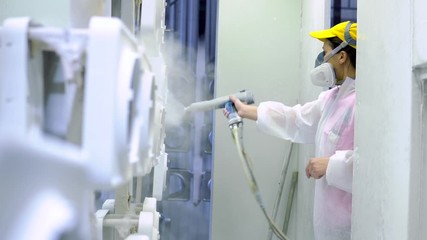 Powder coating of metal parts. Woman in protective suit sprays white powder paint from gun on metal products