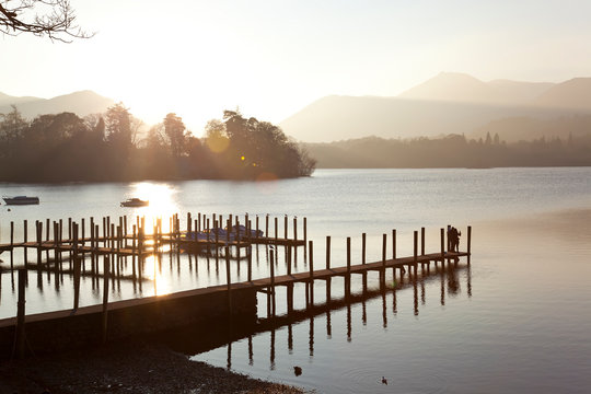 Young couple on pier, sunset, Derwent Water, Lake District, Cumbria, UK