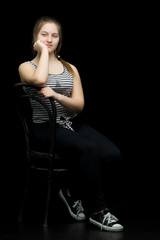 Charming girl teenager sitting on a chair in the studio on a bla