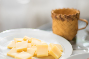 Cheese sliced in a plate, wicker mug on the glass table.