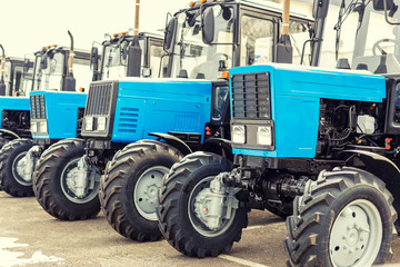 Many different tractors standing in row at agricultural fair for sale outdoors.Equipment for agriculture.Heavy industrial machines presented to an agricultural exhibition