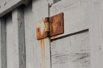 An old, rusty hinge on a white wooden door.