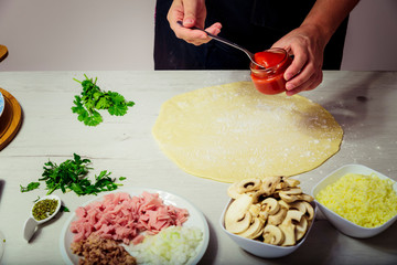 Woman adding ingredients to homemade pizza dough. cooking concept.