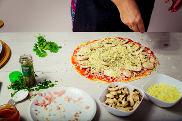 Woman adding ingredients to homemade pizza dough. cooking concept.