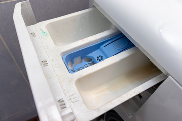 Dirty moldy washing machine detergent and fabric conditioner dispenser drawer compartment close up. Mold, rust and limescale in washing machine tray. Home appliances periodic maintenance