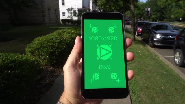 A man walks in a residential neighborhood while holding a smartphone. Green screen with tracking points for your custom content. Generic device.	 	