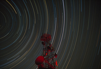 Long-exposure star trails behind a communications tower.