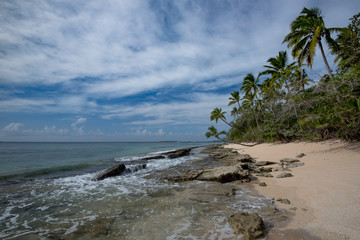Deserted sandy beach on an uninhabited island with palm trees and clouds, Kingdom of Tonga.
