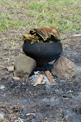 Melanesia, Papua New Guinea, Dobu Island. Typical pottery crock over open fire cooking fish and vegetables covered with palm leaves to steam the meal.