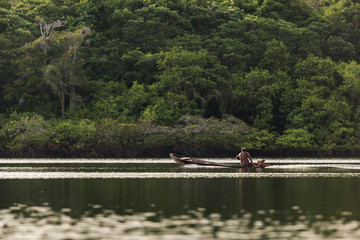 Fototapeta na wymiar Man in a wooden motorized canoe speeds across the Amazon River with thick jungle in the background near Manaus, Brazil