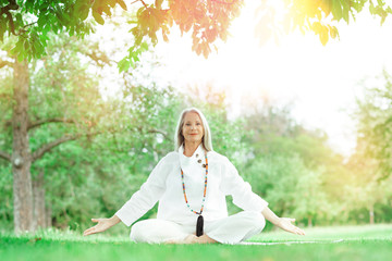 beautiful best age Senior woman with long grey hair doing yoga exercises outdoors