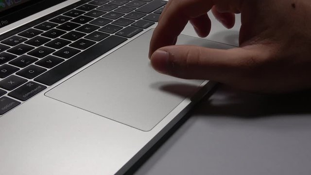 4K. Close-up of the hands of a man using the touch pad and keyboard of a laptop. The hands are close.