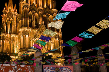 Fototapeta premium Mexico, San Miguel de Allende. Festival banners fly at night in front of illuminated La Parroquia Catholic church.