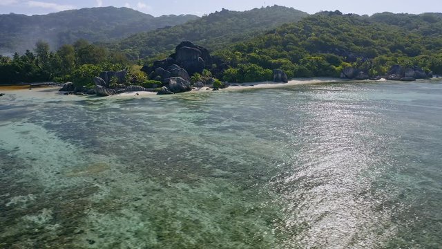 Aerial footage circling around granite boulders on famous Anse Source d'Argent tropical beach. Sunshine reflection on lagoon water surface. La Digue Island, Seychelles