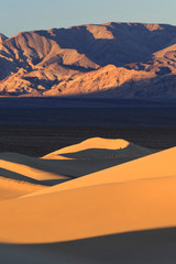 Fototapeta na wymiar Hikers walk during sunrise along the ridgeline of a sand dune in the Mesquite Dunes complex inside Death Valley National Park.