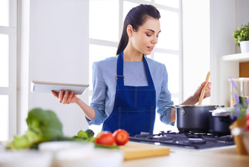Young woman using a tablet computer to cook in her kitchen