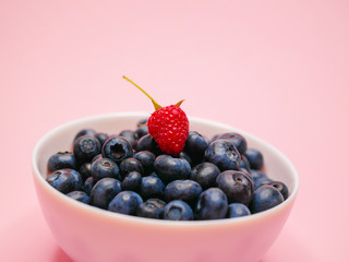 Blueberries on a plate. on a guards, pink background. from the top is a raspberry berry. concept of vitamins, berries. Breakfast ripe, large blueberries. Horizontal. side view