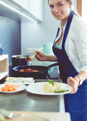 Young woman standing by the stove in the kitchen