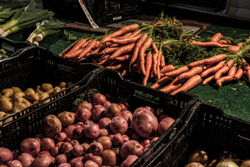 Fresh bunles of carrots with the greenery on top. Red and golden small potatoes in tubs. Vegies highlighted with LED's after sunset.