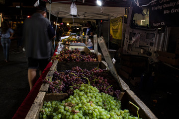 Long table of fruits and vegetables for sale. Lit by LED's to highlight their frshness & color, just after sunset.