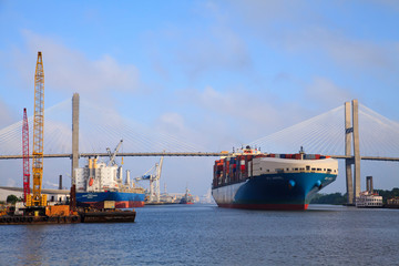 USA, Savannah, Georgia. Construction along the Savannah River near cable-stayed bridge with cargo ship leaving port.