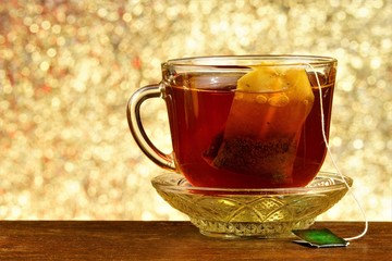Tea in a bag in a Cup on a saucer, background rainbow lights bokeh. Helpful tea is popular refreshing drink obtained by boiling and macerating the leaf of the tea Bush. Quenches thirst well.