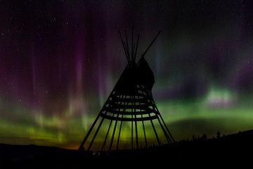 Aurora borealis over tipi display on Blackfeet Tribal Land near St. Mary, Montana, USA