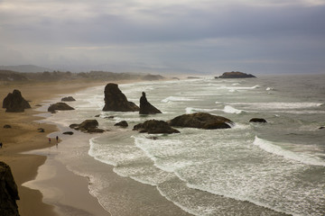 Bandon, Oregon. Face Rock State Scenic Viewpoint, people walking the beach to watch the dramatic surf crash against the haystack rocks,