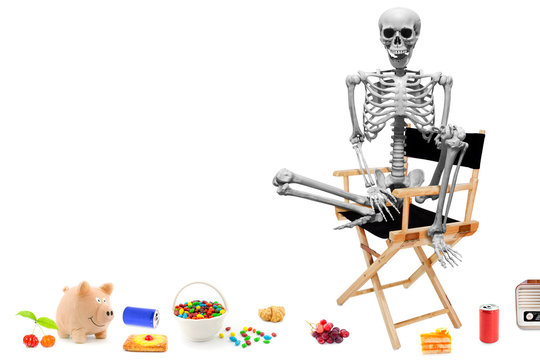 Fake human skeleton sitting on director chair with various items on the floor.halloween concept.