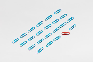 A bunch of blue paperclips aligned and one red paperclip nonaligned on white background , shot from...