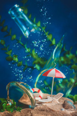Beach umbrella and deck chair underwater with bubbles and seaweeds. Drowning cities and global warming concept. Conceptual still life with miniatures.