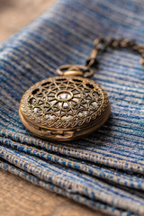 Pocket watch sitting on top of a blue cloth. The time on the pocket watch is 3:49.