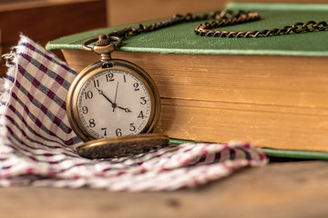 Pocket watch sitting on top of a plaid cloth with a book on the side. The time on the pocket watch...